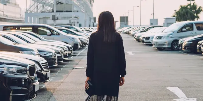 Person walking through a parking lot filled with cars.